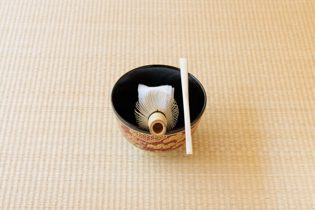畳の上に置かれた裏千家ゆかりの茶道具一式（黒塗の茶碗、茶筅、茶杓）と高級感ある意匠